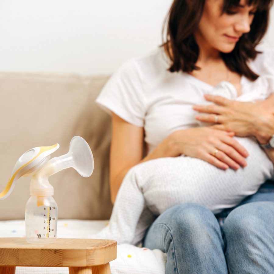 Mom gently looks at the baby and breastfeeds, next to the table is a breast pump for breast milk.