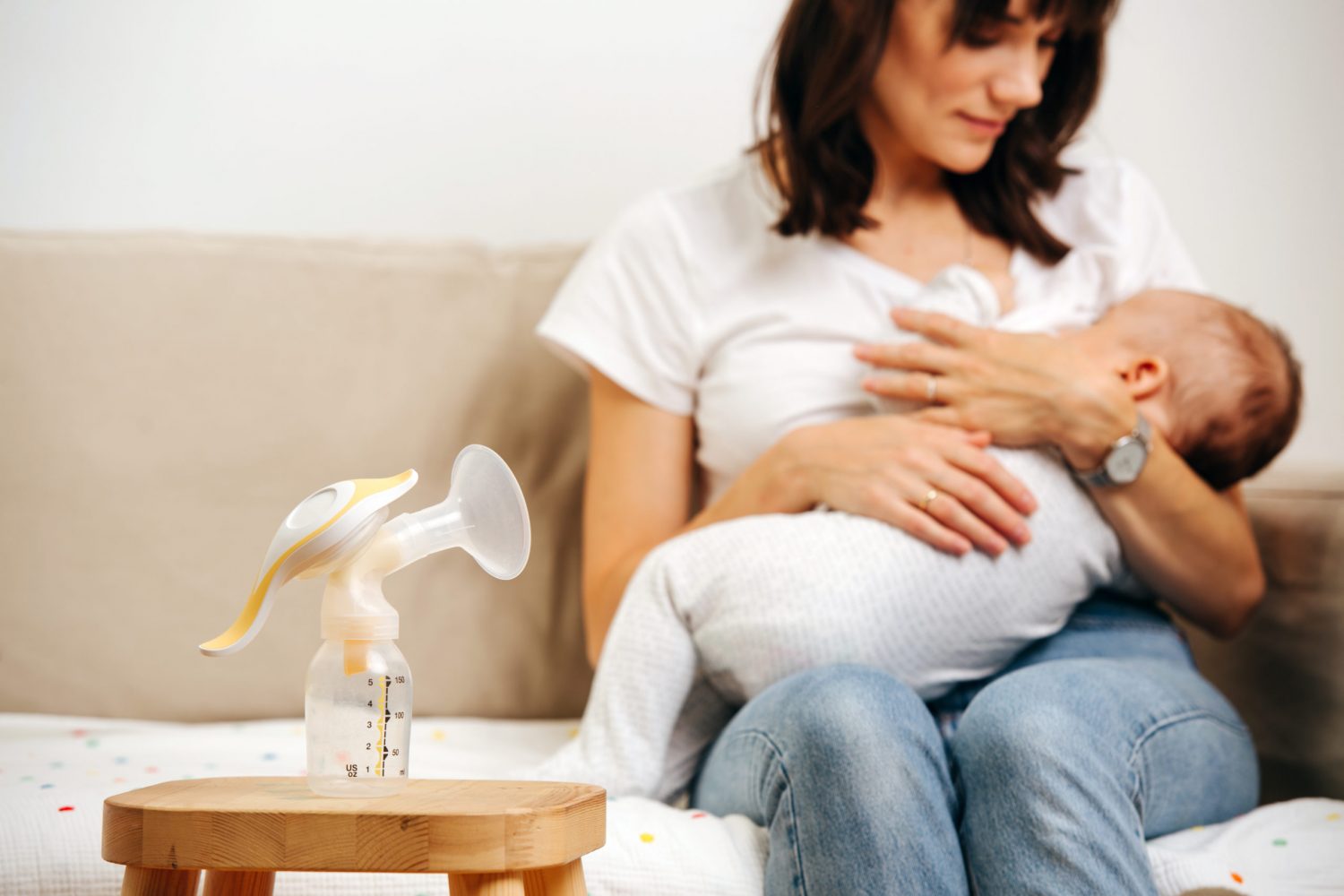 Mom gently looks at the baby and breastfeeds, next to the table is a breast pump for breast milk.