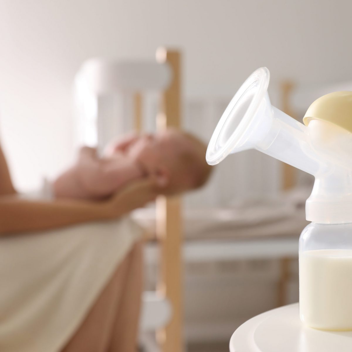 Mother and little baby indoors, focus on table with breast pump